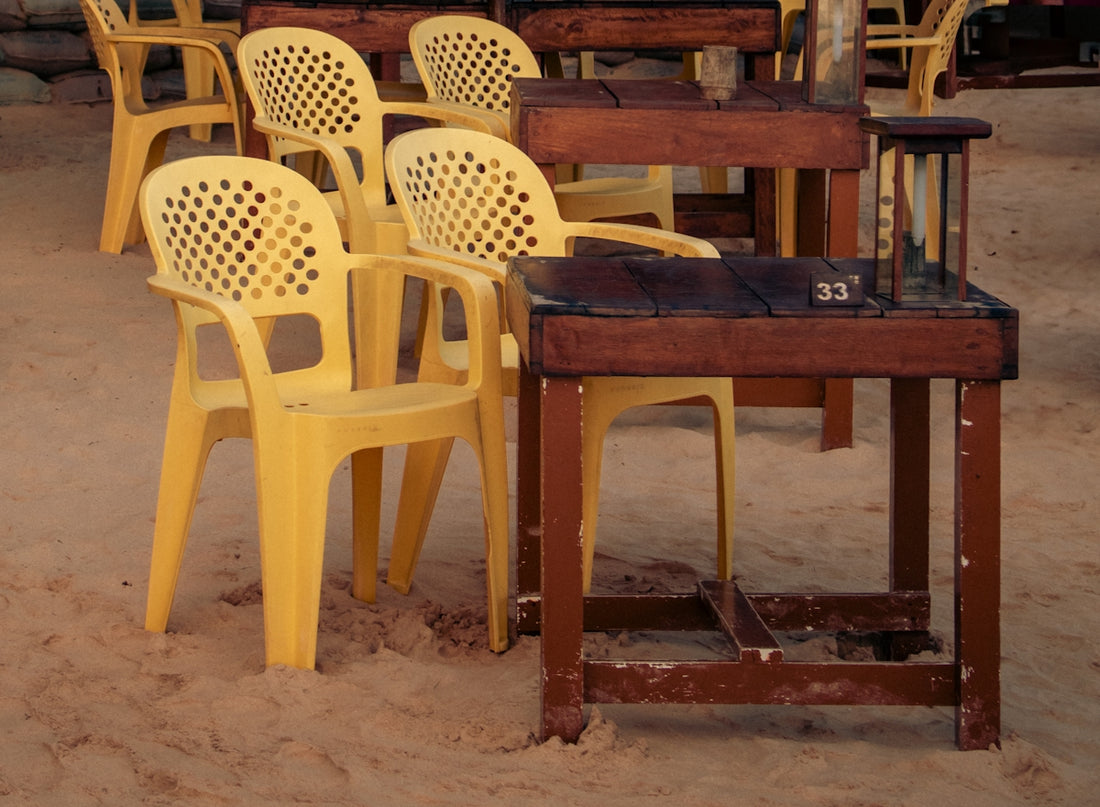 Yellow chairs surround tables on a sandy surface.